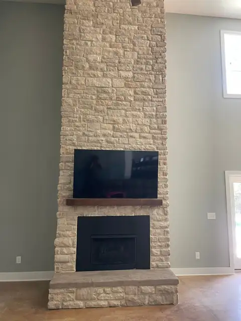 Tall ledgestone fireplace with a mantel and TV above