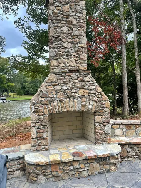 Fieldstone outdoor fireplace with a raised stone hearth, lake in the background