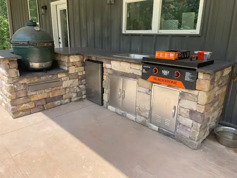 Outdoor kitchen with stainless doors and a griddle, faced in stacked stone