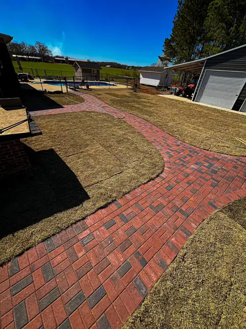 Curving red paver walkway through a new lawn