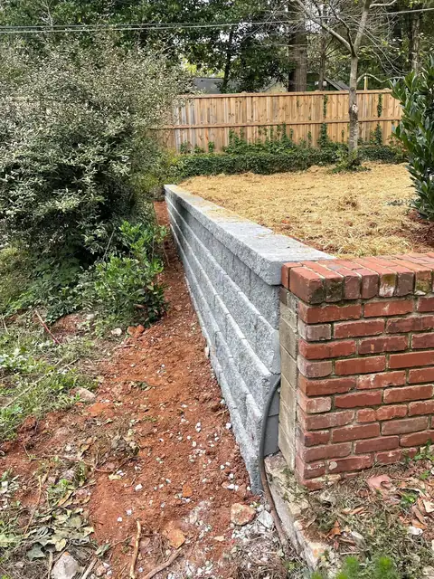 Block retaining wall with a brick return along a fence line